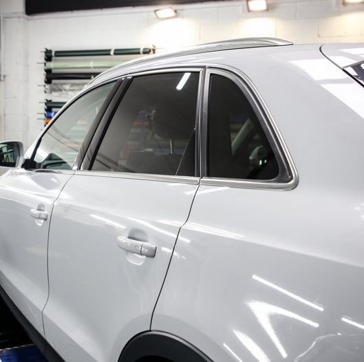 Side view of a white car in a workshop, focusing on the rear passenger door and window.