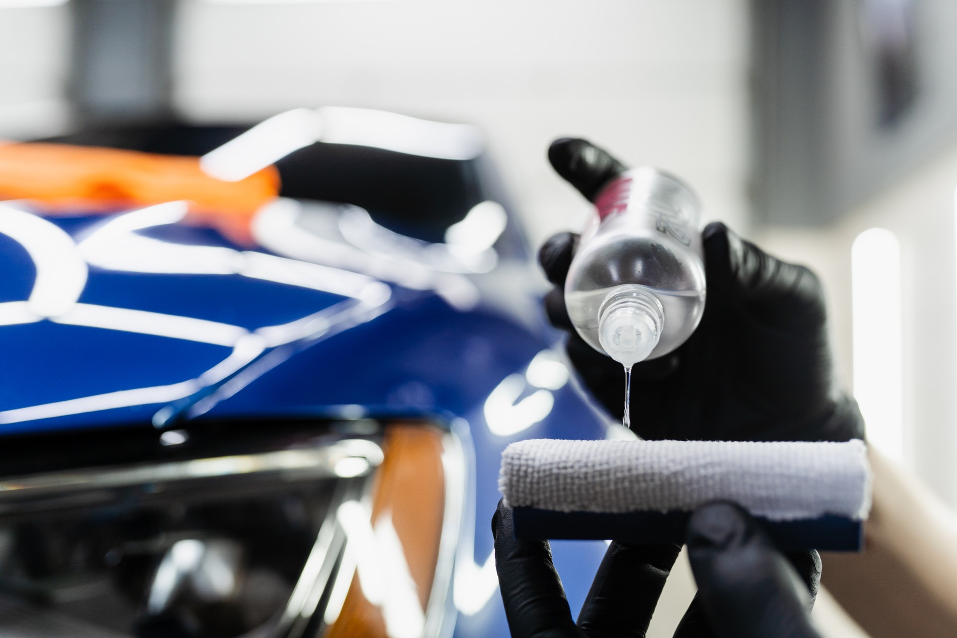 Detailing service worker applies ceramic protective liquid on sponge close-up. Process of pouring ceramic liquid from bottle on sponge to apply protective coating on car.